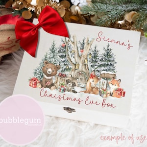 May include: A white wooden box with a watercolour illustration of a snowy forest scene with animals. The box has a red bow and the text "Sienna's Christmas Eve Box" in red lettering. The text "bubblegum designsuk" is in pink lettering on a pink circle.