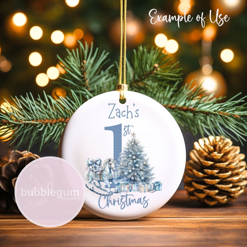 K&ouml;nnte beinhalten: Ein wei&szlig;er Weihnachtsbaumschmuck aus Keramik mit einer blauen und wei&szlig;en Illustration eines Schaukelpferdes, eines Weihnachtsbaums und Geschenken. Der Schmuck ist mit dem Text "Zach's 1st Christmas" personalisiert.