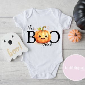 May include: White baby onesie with a cute cartoon pumpkin with a smiling face and the text "the BOO crew".