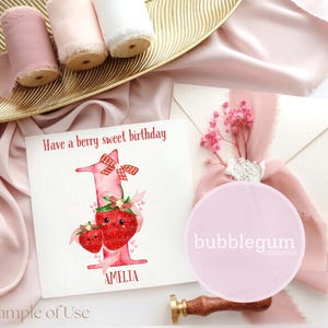 May include: A birthday card with the text "Have a berry sweet birthday" and the name "Amelia". The card features a watercolor illustration of a number one with strawberry details. Pink ribbons and a pink circle with text are also present.