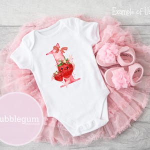 May include: A white short-sleeved baby bodysuit featuring a graphic of the number one decorated with red strawberries, a red and white checkered bow, and small hearts, paired with a pair of light pink sandals with floral accents.