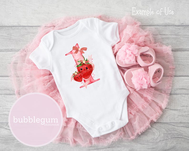May include: A white short-sleeved baby bodysuit featuring a graphic of the number one decorated with red strawberries, a red and white checkered bow, and small hearts, paired with a pair of light pink sandals with floral accents.