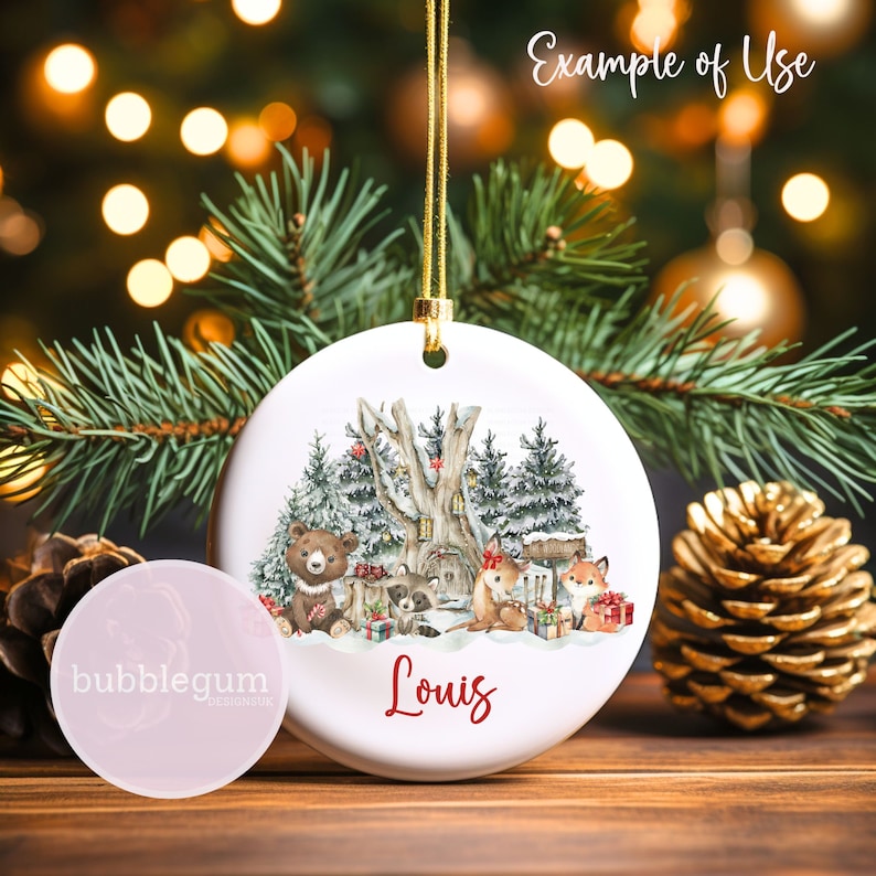 May include: A white ceramic Christmas bauble featuring a winter woodland scene with a bear, raccoon, fox, and deer. The bauble is personalised with the name "Louis".