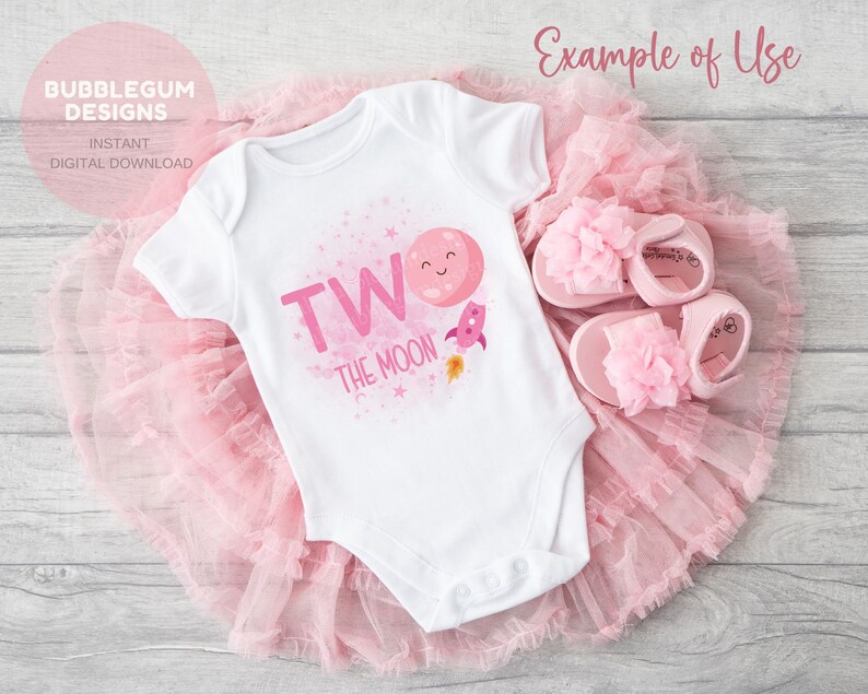 May include: A white onesie with pink lettering that says "Two the Moon" with a pink rocket and a pink moon with a smiling face. The onesie is on a pink tulle skirt.