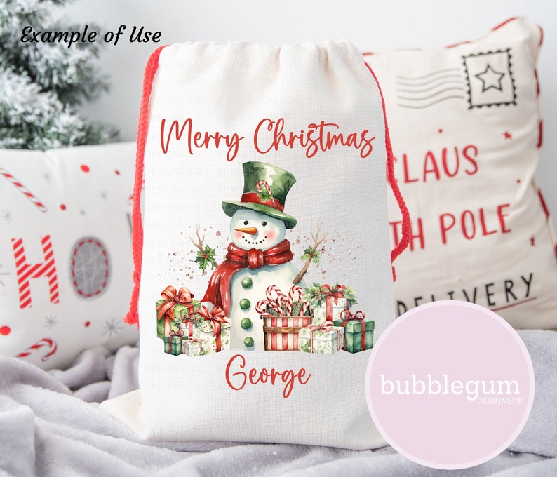 May include: A white canvas drawstring bag with a red drawstring. The bag features a watercolor illustration of a snowman with a green hat, red scarf, and candy canes. The text "Merry Christmas George" is printed on the bag.
