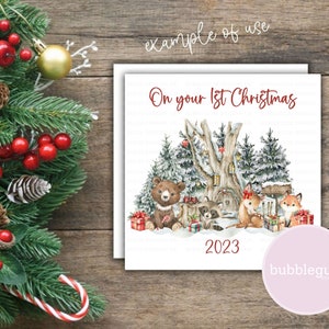 May include: A white card with a winter woodland scene featuring a bear, raccoon, and two foxes. The card says "On your 1st Christmas 2023" in red text.