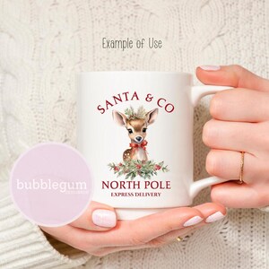 K&ouml;nnte beinhalten: Wei&szlig;e Keramiktasse mit einer roten und wei&szlig;en Illustration eines Rehs mit einer roten Schleife. Der Text "SANTA & CO NORTH POLE EXPRESS DELIVERY" ist in Rot auf die Tasse gedruckt.