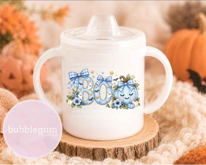 May include: A white sippy cup with two handles and a clear lid, featuring a graphic of the word BOO in light blue plaid letters, decorated with small ghosts, bats, stars, blue flowers, and a light blue plaid pumpkin with a smiling face.