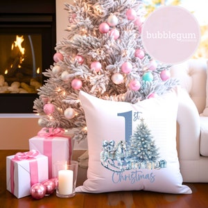 K&ouml;nnte beinhalten: Ein wei&szlig;es Kissen mit einer blauen und wei&szlig;en Illustration eines Schaukelpferdes, das einen Weihnachtsbaum mit Geschenken zieht. Das Kissen tr&auml;gt den Text "1. Weihnachten".