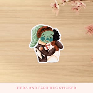 May include: A sticker featuring a watercolor illustration of two characters embracing. One character has green skin, a brown aviator cap, and a white and brown outfit. The other character has black hair and a brown outfit. The sticker's text reads "HERA AND EZRA HUG STICKER."