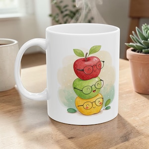 Può includere: Tazza in ceramica bianca con un disegno di tre mele dei cartoni animati, ognuna con gli occhiali. La mela in alto è rossa, quella centrale è verde e quella in basso è gialla. Il design è in stile acquerello con uno sfondo verde chiaro e giallo.