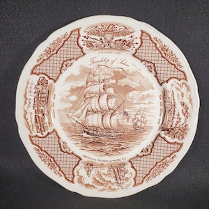 May include: A brown and white ceramic plate with a decorative design featuring a ship, the text "Friendship of Salem", and the words "Canton Net 1830", "New York Harbor 1830", and "U.S. Delaware Capturing Le Croyable".