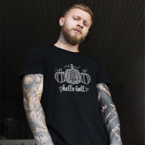 May include: A black t-shirt with a white graphic of three pumpkins and the text "hello fall" in a cursive font.