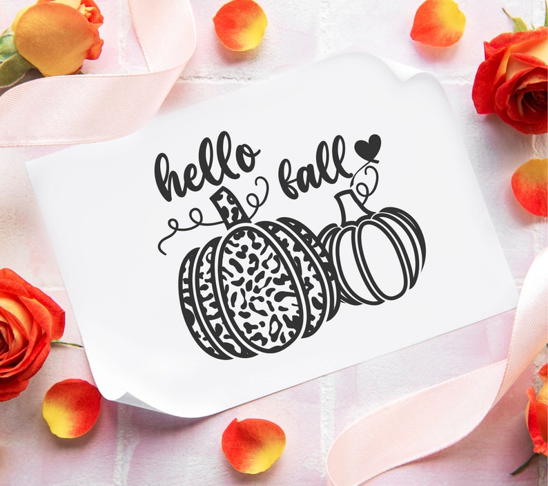 May include: A white card with the text "hello fall" in black script font. Two pumpkins are illustrated below the text. One pumpkin is solid black and the other is patterned with black spots. A small red heart is above the word "fall".