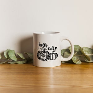 May include: White ceramic mug with a black design of two pumpkins and the text "hello fall" with a heart.