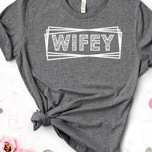 May include: Gray t-shirt with the word "WIFEY" printed in white with a glittery texture inside a white box.