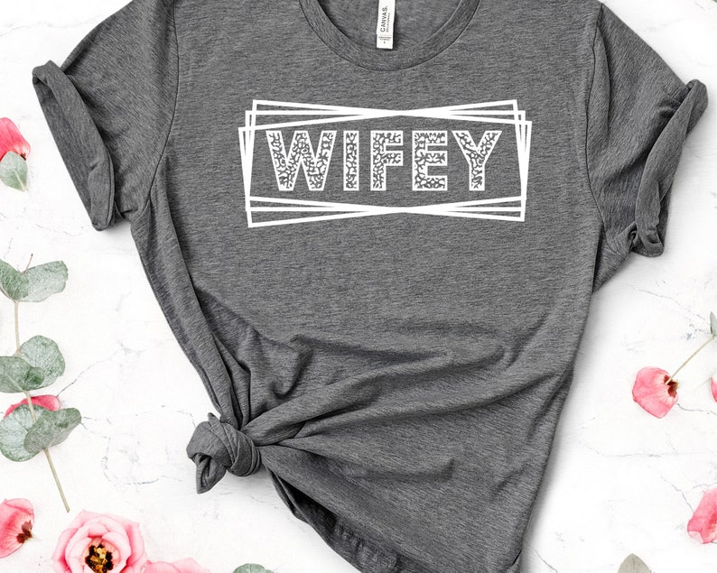 May include: Gray t-shirt with the word "WIFEY" printed in white with a glittery texture inside a white box.