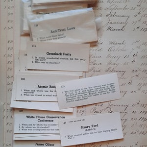 May include: A collection of vintage trivia cards with questions about historical figures and events. The cards are printed on white paper with black text and are arranged in a random order. Some of the cards have handwritten notes on them.