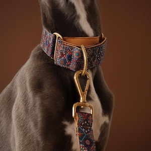 May include: A wide dog collar and matching leash featuring a dark blue fabric with a multi-colored geometric pattern. The collar has a tan leather inner lining and gold-toned metal hardware, including a D-ring and a swivel snap hook on the leash.