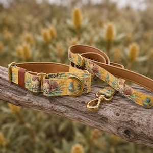 May include: A yellow pet collar and matching leash featuring a botanical print of protea flowers and eucalyptus leaves. The set includes gold-toned metal hardware, including a D-ring and a swivel snap hook, with a tan interior lining.