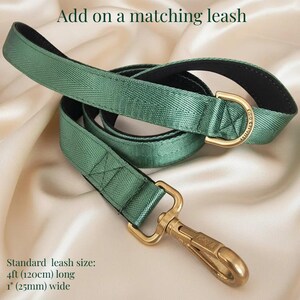 A green leash with a gold (brass) metal buckle and hook is displayed on a beige fabric background.