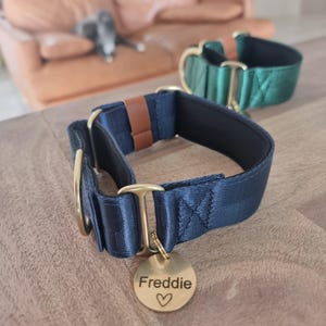 May include: A navy blue dog collar with gold-toned metal hardware, a brown leather-like accent, and a round gold-toned metal tag engraved with the name Freddie and a heart symbol. A second green dog collar is visible in the background.