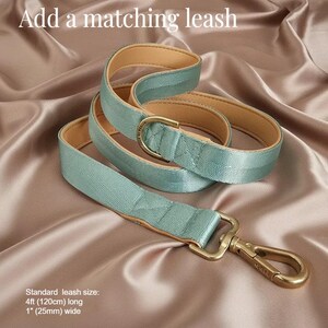 A sage green dog leash with a gold-colored metal attachment is displayed on a satin background