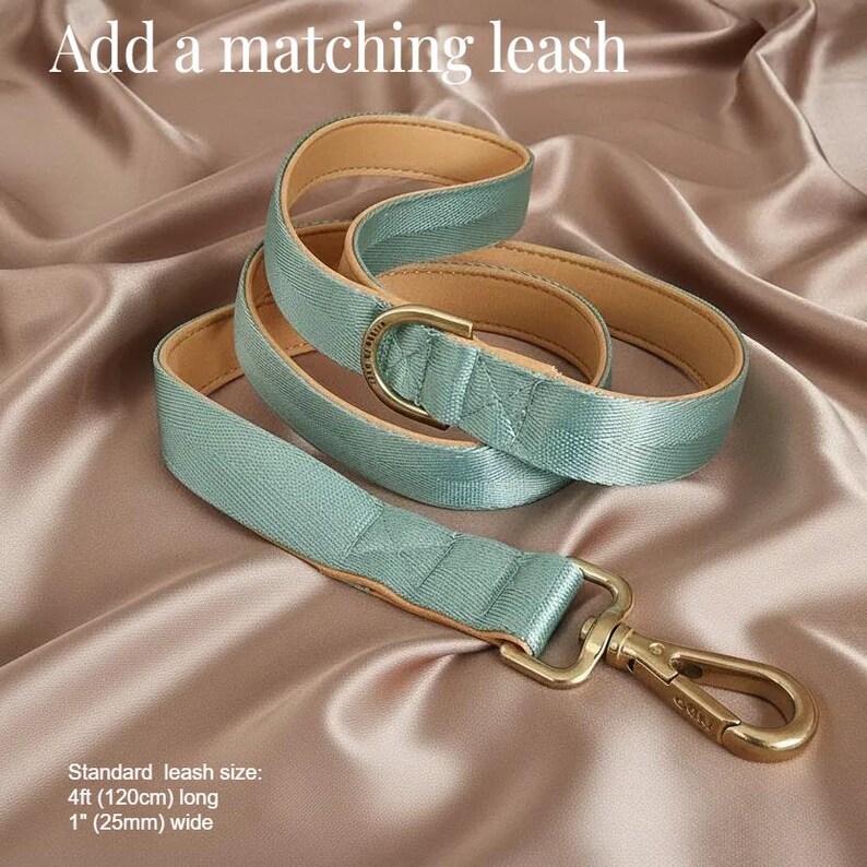 A sage green dog leash with a gold-colored metal attachment is displayed on a satin background