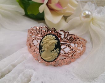 May include: Rose gold filigree cuff bracelet with an oval cameo. The cameo features a cream-colored profile against a black background. The bracelet has an openwork design with floral and geometric patterns.