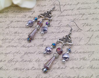 May include: Dangle earrings with silver-tone filigree tops and multiple strands of iridescent beads in shades of purple, silver, and iridescent colors. The earrings have a vintage, bohemian style.