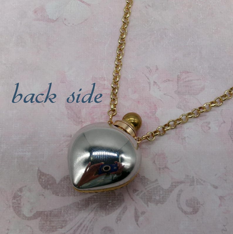 May include: A silver-colored, heart-shaped pendant necklace with a gold-colored chain. The pendant has a reflective surface and a small gold-colored cap. The words "back side" are printed in blue on the background.
