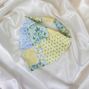 May include: A patchwork headband with a variety of floral and geometric patterns in yellow, blue, and white. The headband is made of fabric and has an elastic band for a comfortable fit. The background is a white satin fabric.