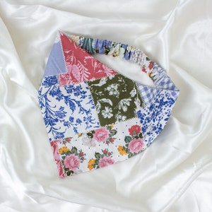 May include: A patchwork headband featuring various floral and patterned fabrics in shades of red, blue, green, and white. The headband has an elastic band for a comfortable fit. The design includes floral, paisley, and gingham patterns.