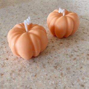 May include: Two small orange pumpkin-shaped candles with white wicks.