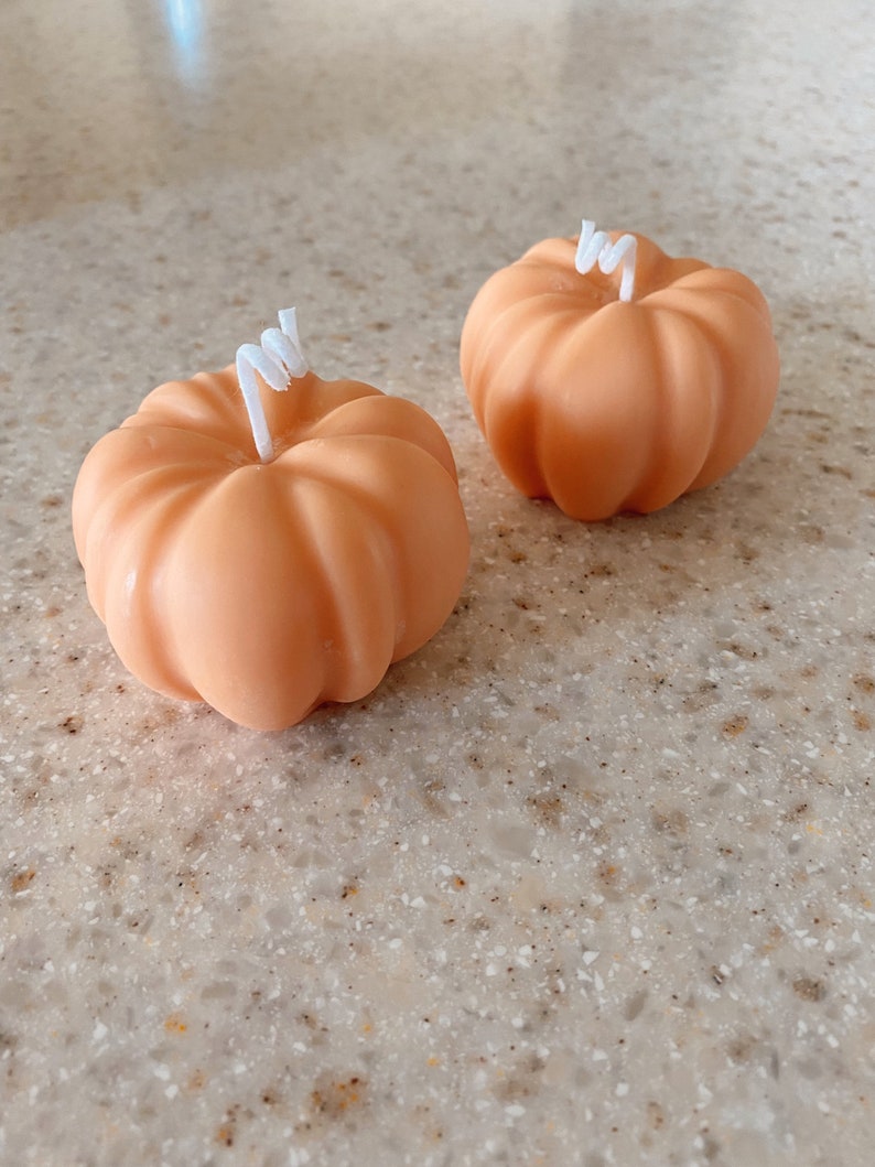 May include: Two small orange pumpkin-shaped candles with white wicks.