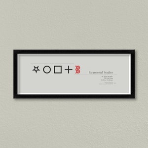 May include: A black framed print with a white background. The print features a black star, circle, square, and plus sign, along with a red wavy line. The text "Paranormal Studies" is in black, and the text "Dr. Egon Spengler", "Dr. Ray Stantz", and "Dr. Peter Venkman" is in red.