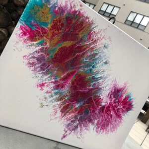 Op de afbeelding: Abstracte acryl gietverf op een wit canvas. Het kunstwerk toont een dynamische compositie van kleuren, waaronder teal, goud en tinten roze en paars. De verf is gelaagd en getextureerd.