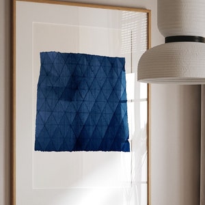 May include: A dining room table with a white marble top and wooden legs. The table is set with a white teapot and two wicker chairs. A large framed print with a blue geometric design hangs on the wall behind the table.
