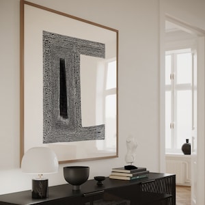 May include: A black metal cabinet with a mesh front and a black top. The cabinet has two doors and is sitting on a wooden floor. There is a white lamp, a black bowl, and a stack of books on top of the cabinet. A framed black and white abstract print hangs on the wall behind the cabinet.