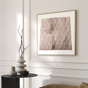 May include: A framed abstract art print with a geometric pattern in shades of pink and brown. The print is hanging on a white wall above a black side table with a vase and decorative objects.