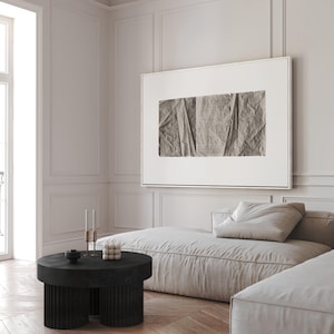 K&ouml;nnte beinhalten: Ein wei&szlig;es, geteiltes Sofa mit einem gro&szlig;en, gerahmten abstrakten Druck dar&uuml;ber. Das Sofa steht in einem Raum mit wei&szlig;en W&auml;nden und einem Holzboden. Ein schwarzer, runder Couchtisch mit einem geriffelten Untergestell steht vor dem Sofa.