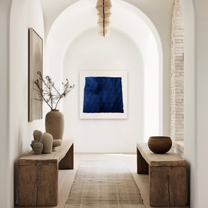 May include: A long, narrow hallway with white walls and arched doorways. The hallway is decorated with a blue abstract painting, a wooden bench, and a vase with dried branches. The floor is made of wood and a rug runs down the centre of the hallway.