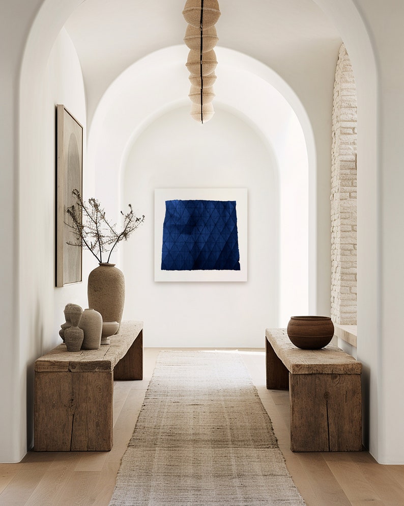 May include: A long, narrow hallway with white walls and arched doorways. The hallway is decorated with a blue abstract painting, a wooden bench, and a vase with dried branches. The floor is made of wood and a rug runs down the centre of the hallway.