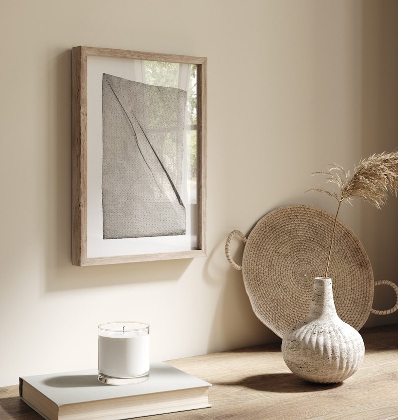 May include: A framed black and white abstract print with a woven tray and a white ceramic vase with a dried plant on a wooden surface.