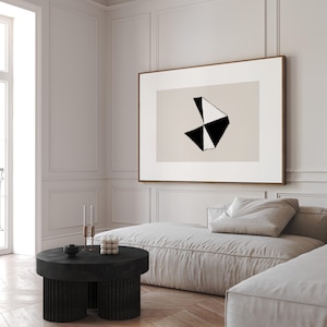 May include: A black and white abstract geometric art print in a wooden frame hangs above a light beige sectional sofa with a black round coffee table. The coffee table has three legs and a textured surface.