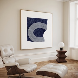 May include: A white leather armchair and ottoman with a dark wood base. A framed abstract art print with a navy blue background and white dots hangs on the wall behind the chair.