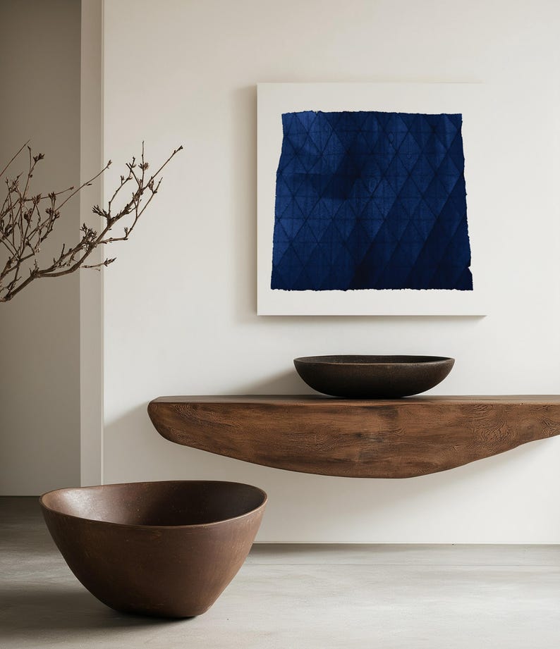 May include: A dark blue abstract painting with a geometric pattern hangs on a white wall above a wooden shelf. Two brown bowls are on the shelf.