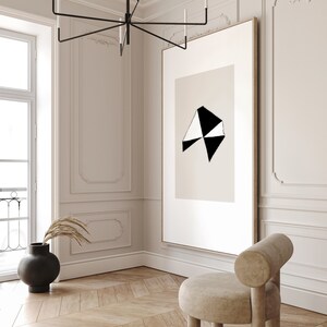 May include: A black and white abstract geometric art print in a simple wooden frame hangs on a white wall in a modern living room. A beige armchair sits in the corner of the room.