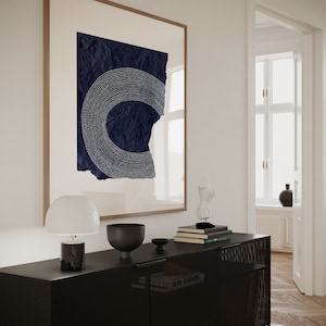 May include: A black metal cabinet with a wire mesh front and a white lamp on the left side. The cabinet is decorated with a black bowl, a stack of books, and a white sculpture. A framed print with a blue and white abstract design hangs on the wall behind the cabinet.