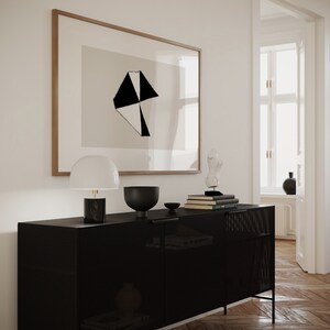 May include: A black metal cabinet with a wire mesh front and two doors. The cabinet is sitting on a wooden floor and has a lamp, a bowl, and books on top of it. There is a framed print of a black and white geometric design on the wall behind the cabinet.
